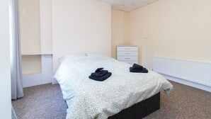 Een slaapkamer met een bed, nachtkastje, dressoir en radiator.