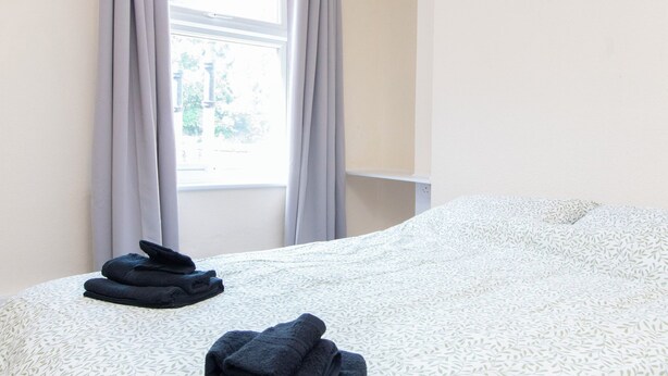 Een hotelkamer met een bed, een raam met gordijnen en uitzicht op groen.