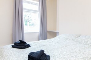 A hotel room with a bed, a window with curtains, and a view of greenery outside. - Brookvale Guest House Room 14 (Southampton)