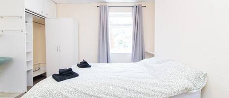 A hotel room with a bed, a wardrobe, a bathroom, and a window with curtains.