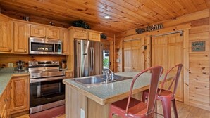 Ein Interieur einer Holzhütte mit Holzwänden, einer Küche mit Edelstahlgeräten, einem Spülbecken und zwei roten Stühlen.