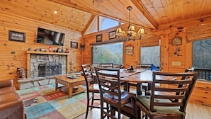 Ein Holzblockhaus-Interieur mit Kamin, Esstisch, Stühlen und einem Fernseher.