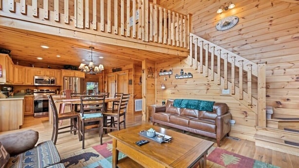 Ein Holzblockhaus mit Essbereich, einer Couch, einer Treppe und einer Küche.