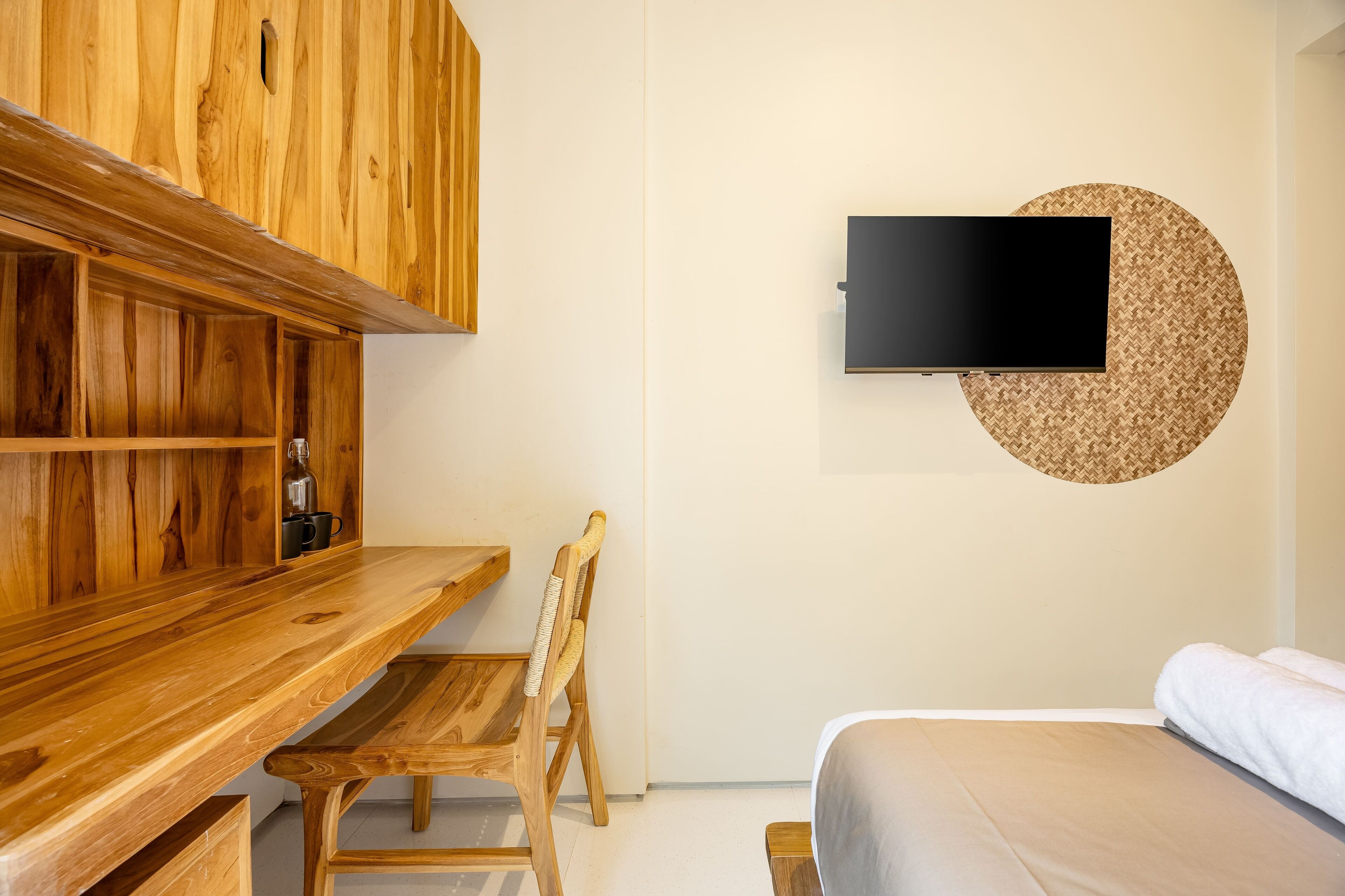Ein Zimmer mit einem Holztisch, einem Sessel, einem Bett und einem an der Wand montierten Fernseher.