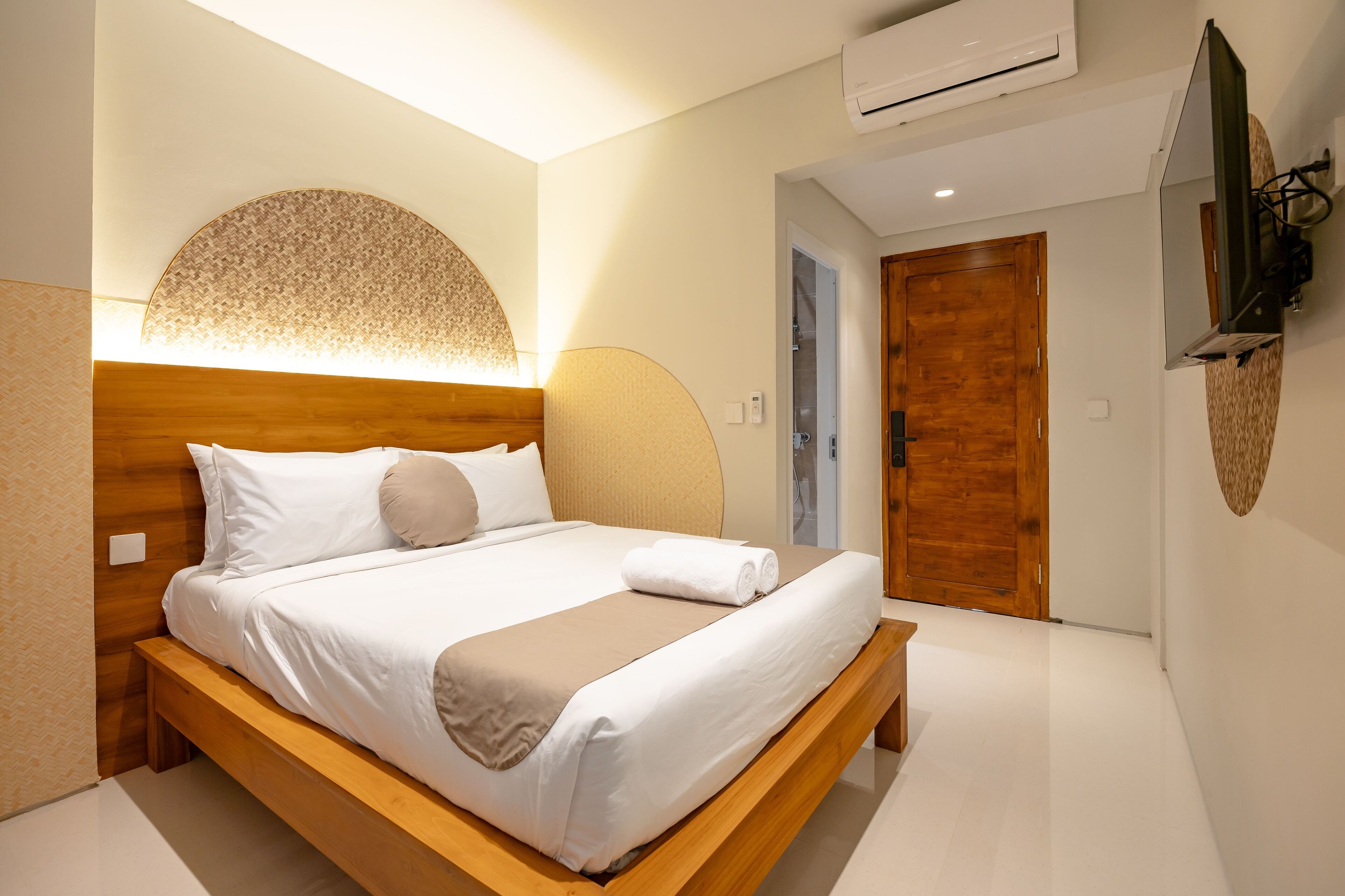 A hotel room with a wooden bed, a large wall-mounted TV, and a wooden door.