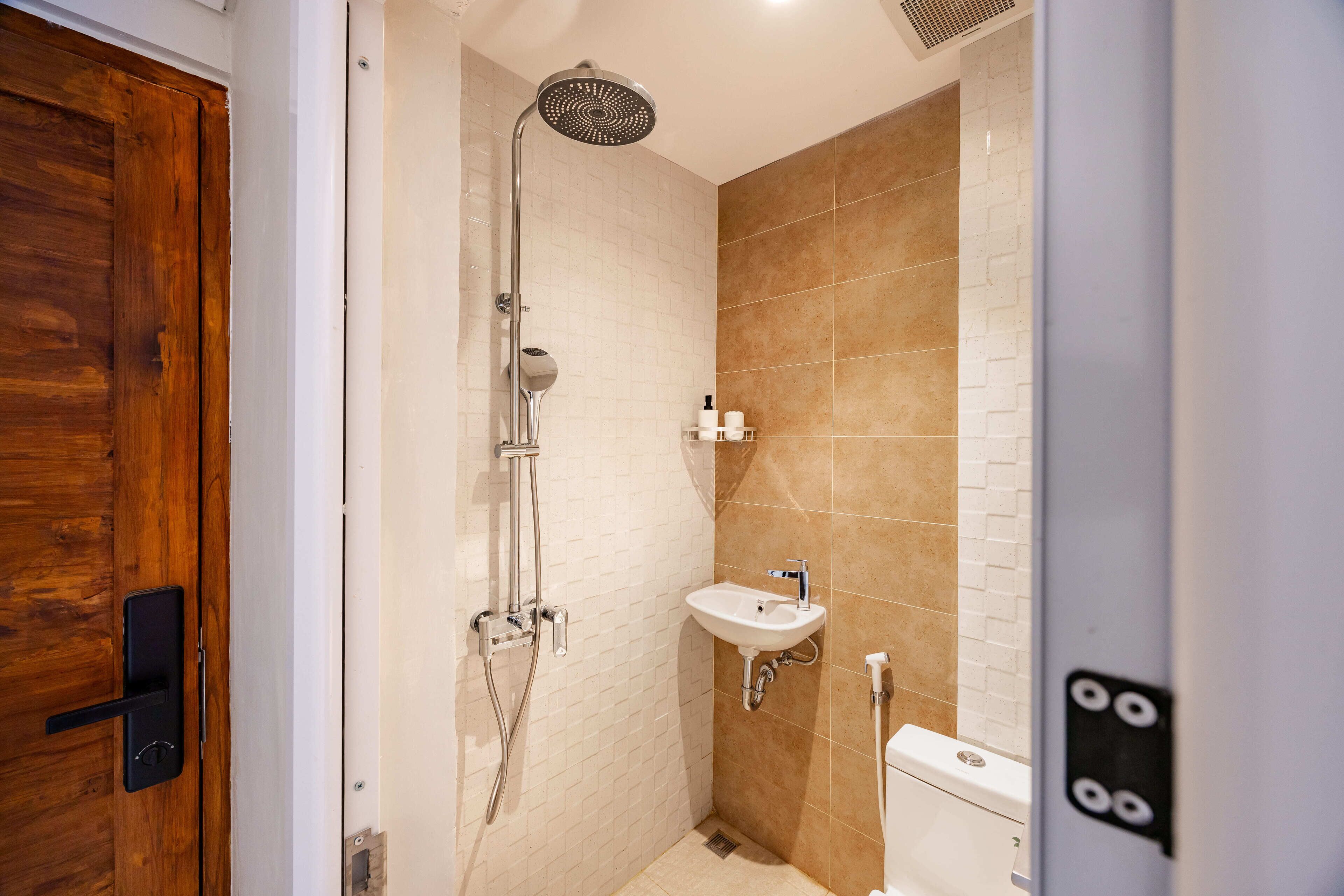 Un baño pequeño con puerta de madera, ducha, lavamanos e inodoro.