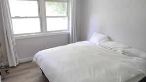 A bedroom with a large bed, a window with curtains, and a wooden floor.