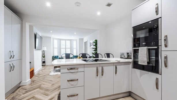 A modern kitchen with white cabinets, a built-in oven, and a herringbone wood floor. - Riverside | Work-Stay | Free Dedicated Parking (Warrington)
