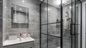 A modern bathroom with a glass-enclosed shower, a vanity with a mirror, and a tiled backsplash. - Riverside | Work-Stay | Free Dedicated Parking (Warrington)