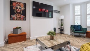 A modern living room with a flat-screen TV, a sofa, a coffee table, and a decorative plant. - Riverside | Work-Stay | Free Dedicated Parking (Warrington)