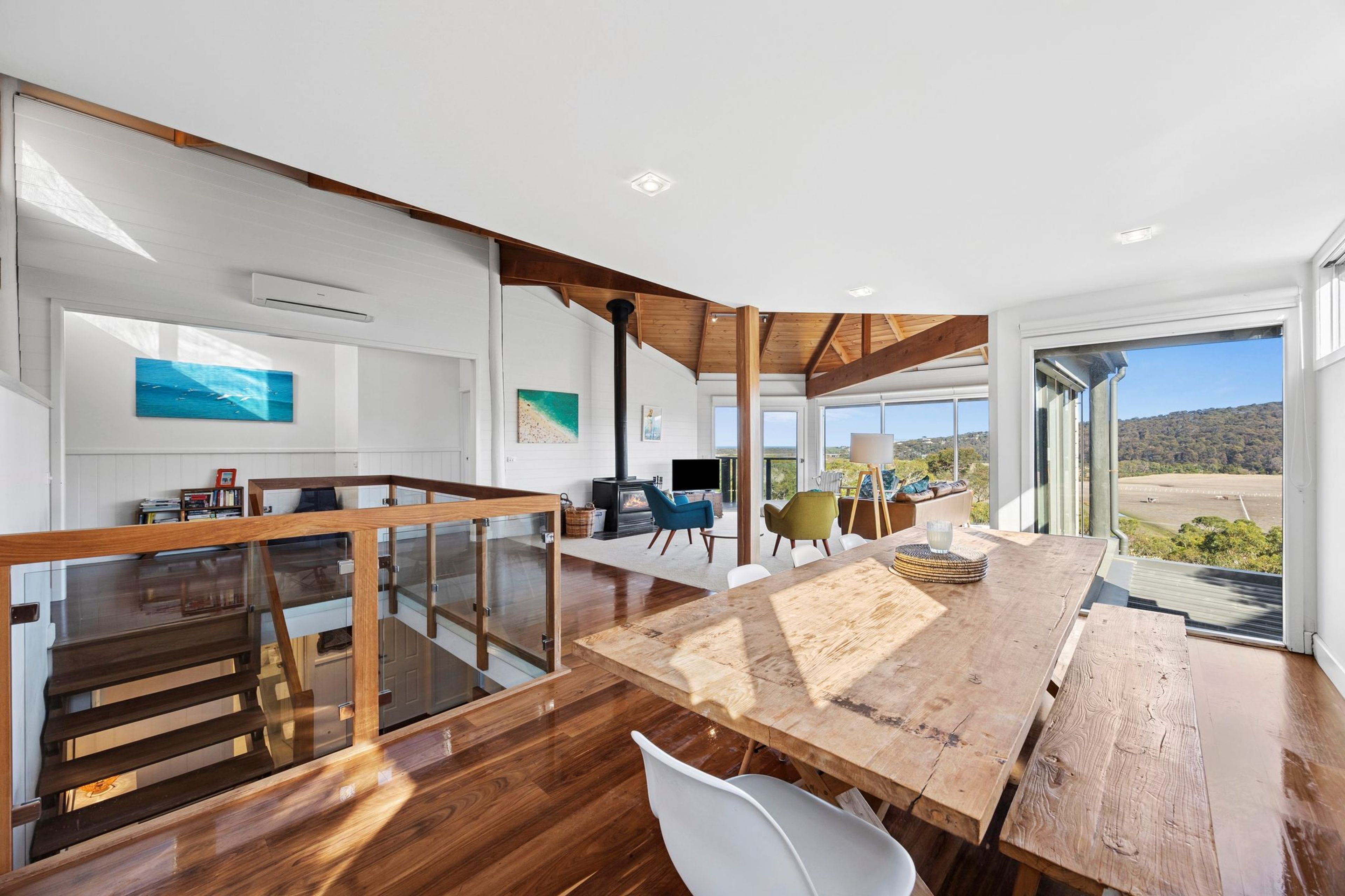 A spacious living area with a wooden dining table, a staircase, and a view of the outdoors.
