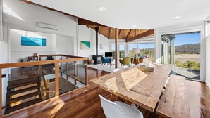 A spacious living area with a wooden dining table, a staircase, and a view of the outdoors. - Panorama Dream (Aireys Inlet)