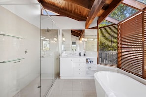 Ein modernes Badezimmer mit Duschkabine aus Glas, einem weißen Waschtisch mit Badewanne und Holzbalkendecke.