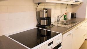 Eine moderne Küche mit einem schwarzen Induktionskochfeld, einer integrierten Kaffeemaschine und einem Spülbecken aus Edelstahl.