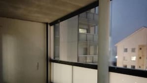Ein Balkon mit Glasbrüstung, einem runden Tisch und zwei Stühlen.