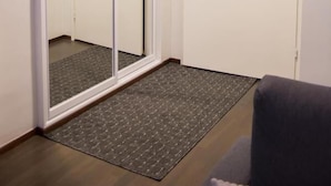 Ein Flur mit einer Schiebetür, einer Fußmatte und einem grauen Sofa.