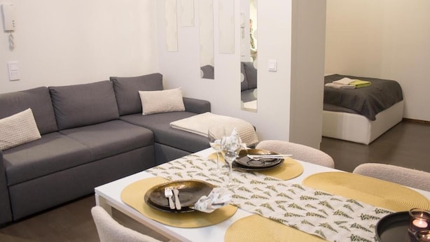 Ein modernes Wohnzimmer mit einem grauen Sofa und einem Esstisch, gedeckt mit Tellern, Gläsern und Besteck.