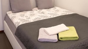 Ein ordentlich bezogenes Bett mit einem gemusterten Überwurf, zwei Kissen und zwei gefalteten Handtüchern.