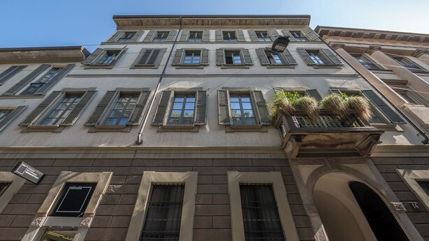 Un edificio de varios pisos con un estilo arquitectónico clásico, que cuenta con un balcón con plantas, varias ventanas y una entrada visible.