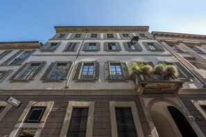 A multi-story building with a classical architectural style, featuring a balcony with plants, multiple windows, and a visible entrance. - Bagutta Suites (Milan)