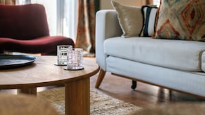 Una mesa redonda de madera con tres vasos transparentes y un plato, una silla roja y un sofá blanco con cojines estampados en una sala de estar.
