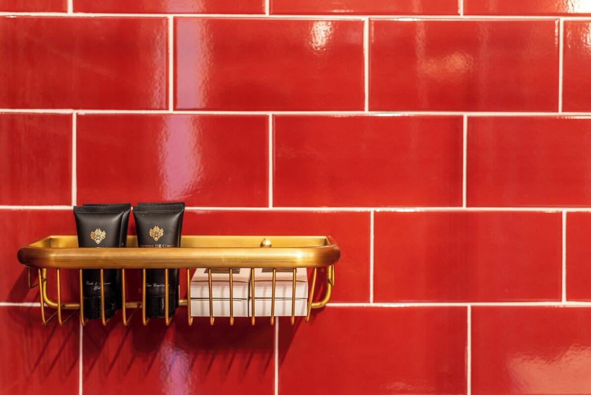 A red tiled wall with a gold tray holding two black toiletry bags and a white container.
