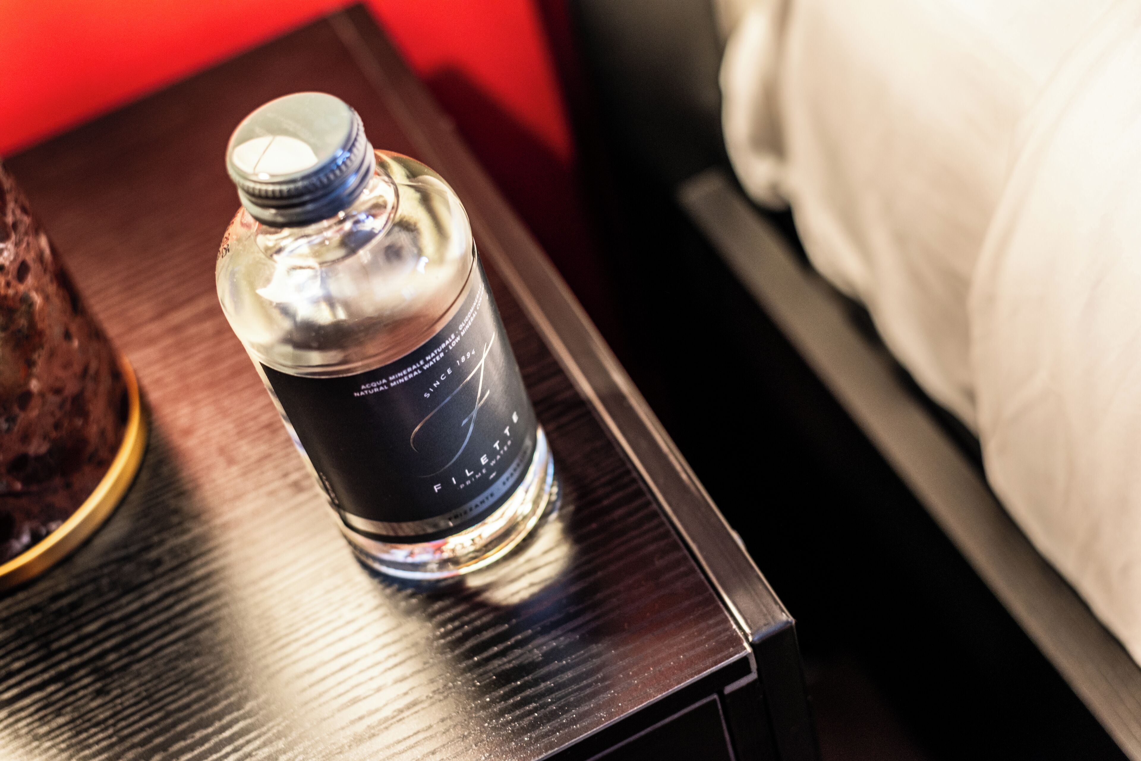 Una botella de agua sobre una mesita de noche de madera junto a la cama.