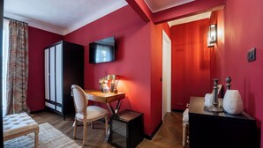 Una habitación con una cama, un escritorio con una silla, un televisor montado en la pared y una pared roja.