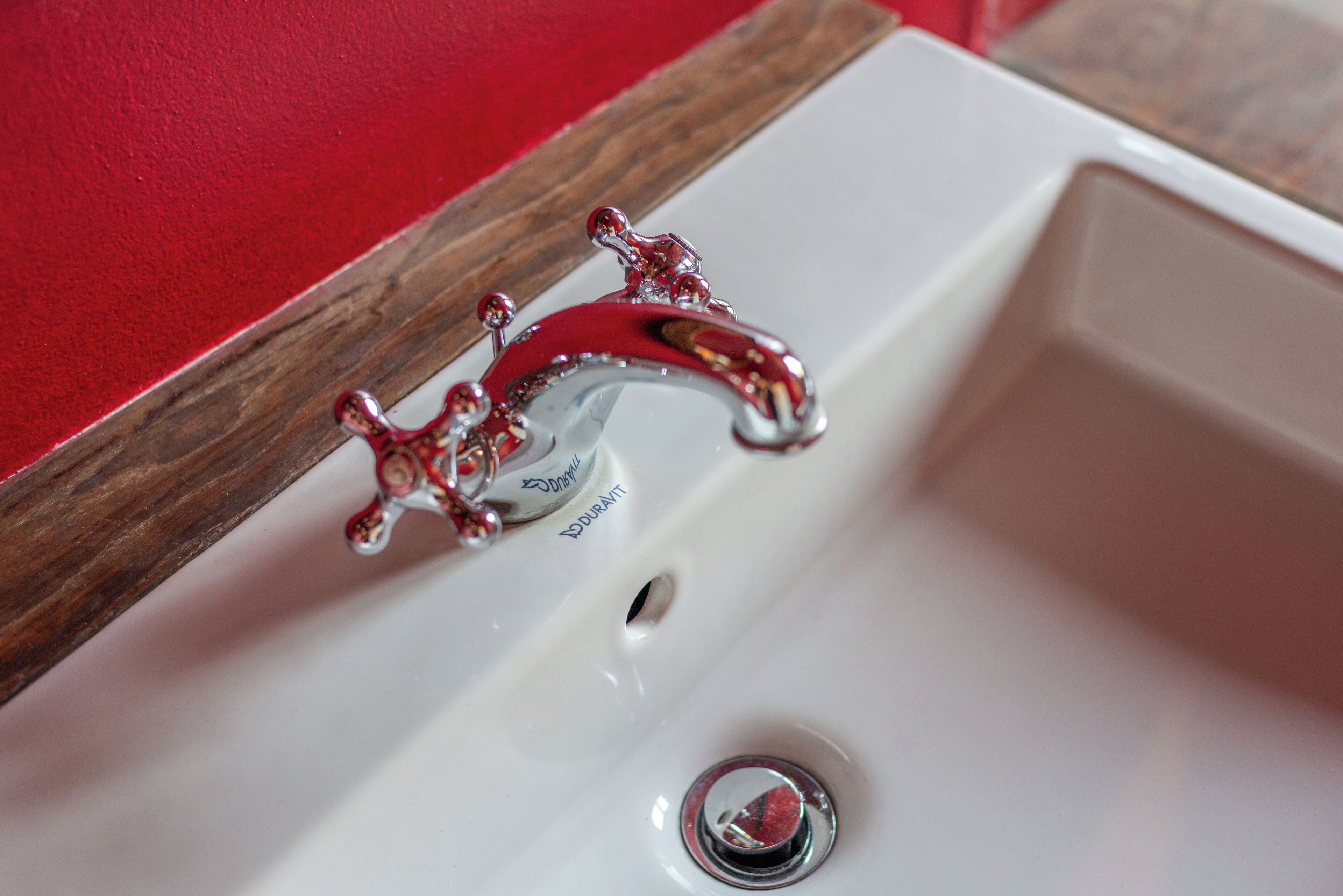 A white bathroom sink with a vintage-style faucet and a wooden frame around the mirror.