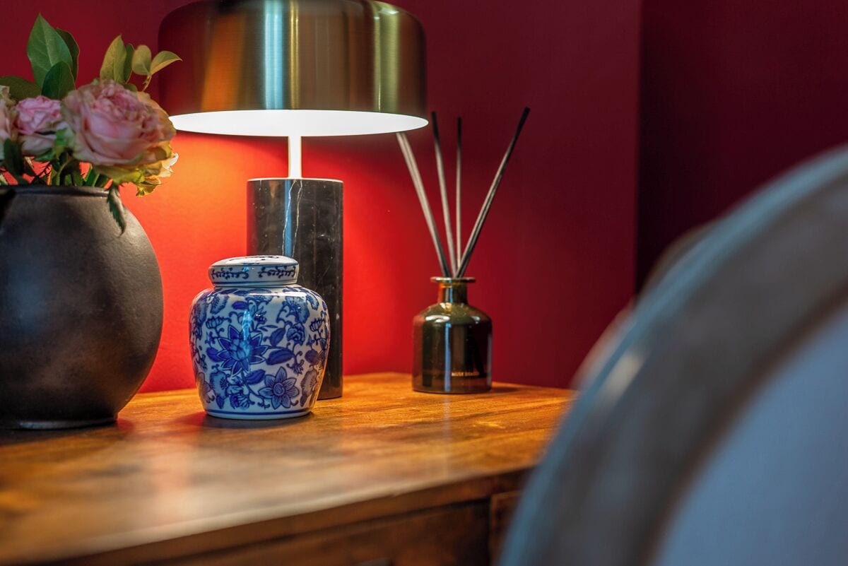 A wooden table with a blue and white ceramic vase, a metal candle holder, and a tall lamp with a white shade.