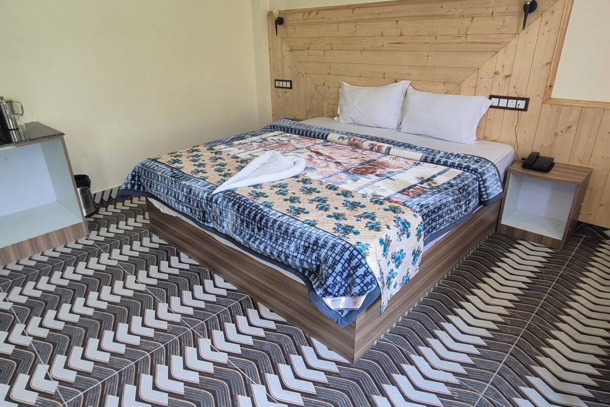 Makuuhuoneessa on puinen sängynpääty, kuviollinen lattia, peitolla varustettu sänky, yöpöytä, jossa on puhelin, ja tuoli.