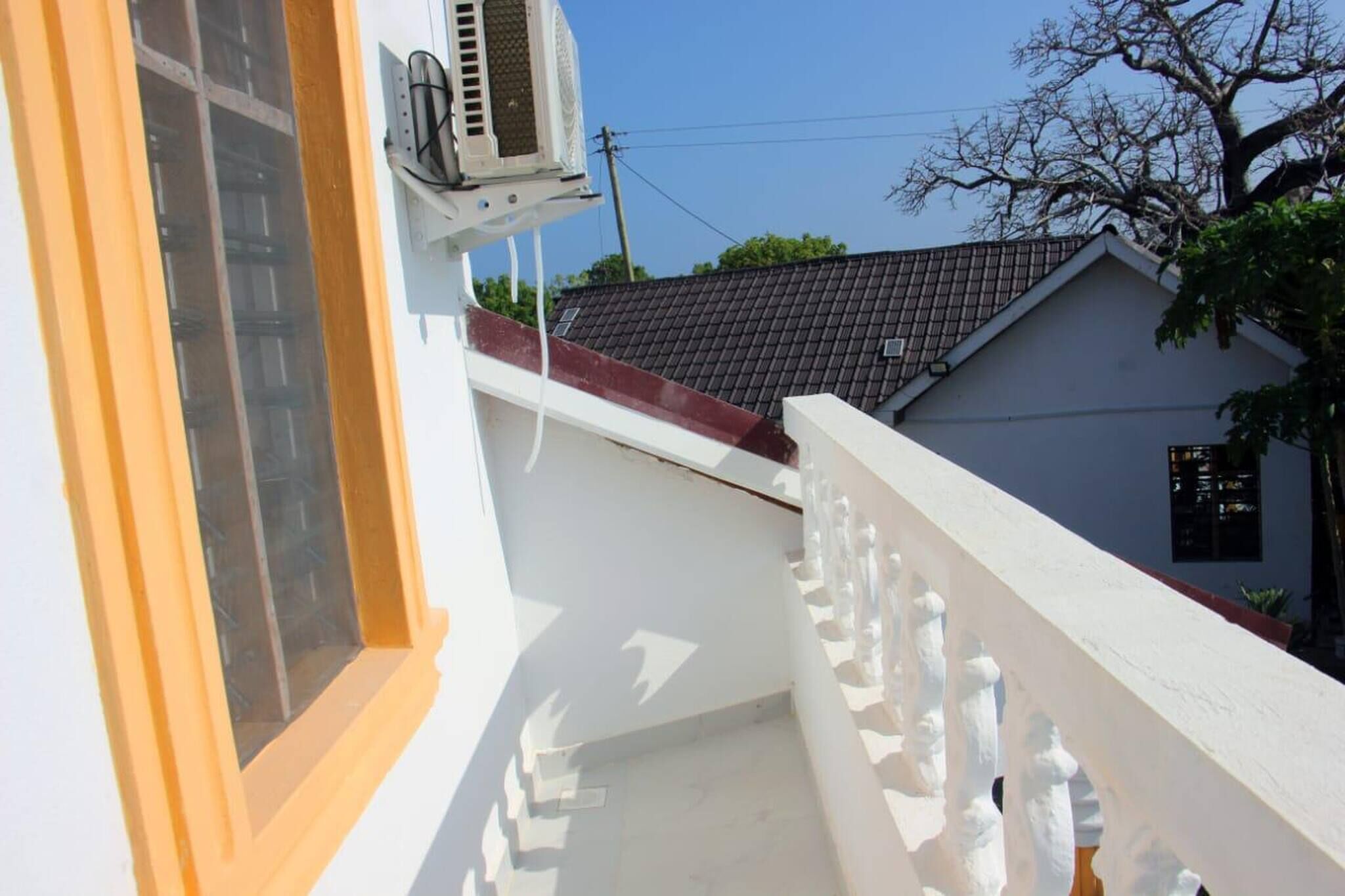 Un bâtiment blanc avec un toit rouge, une fenêtre ornée d’un cadre jaune et une balustrade blanche.