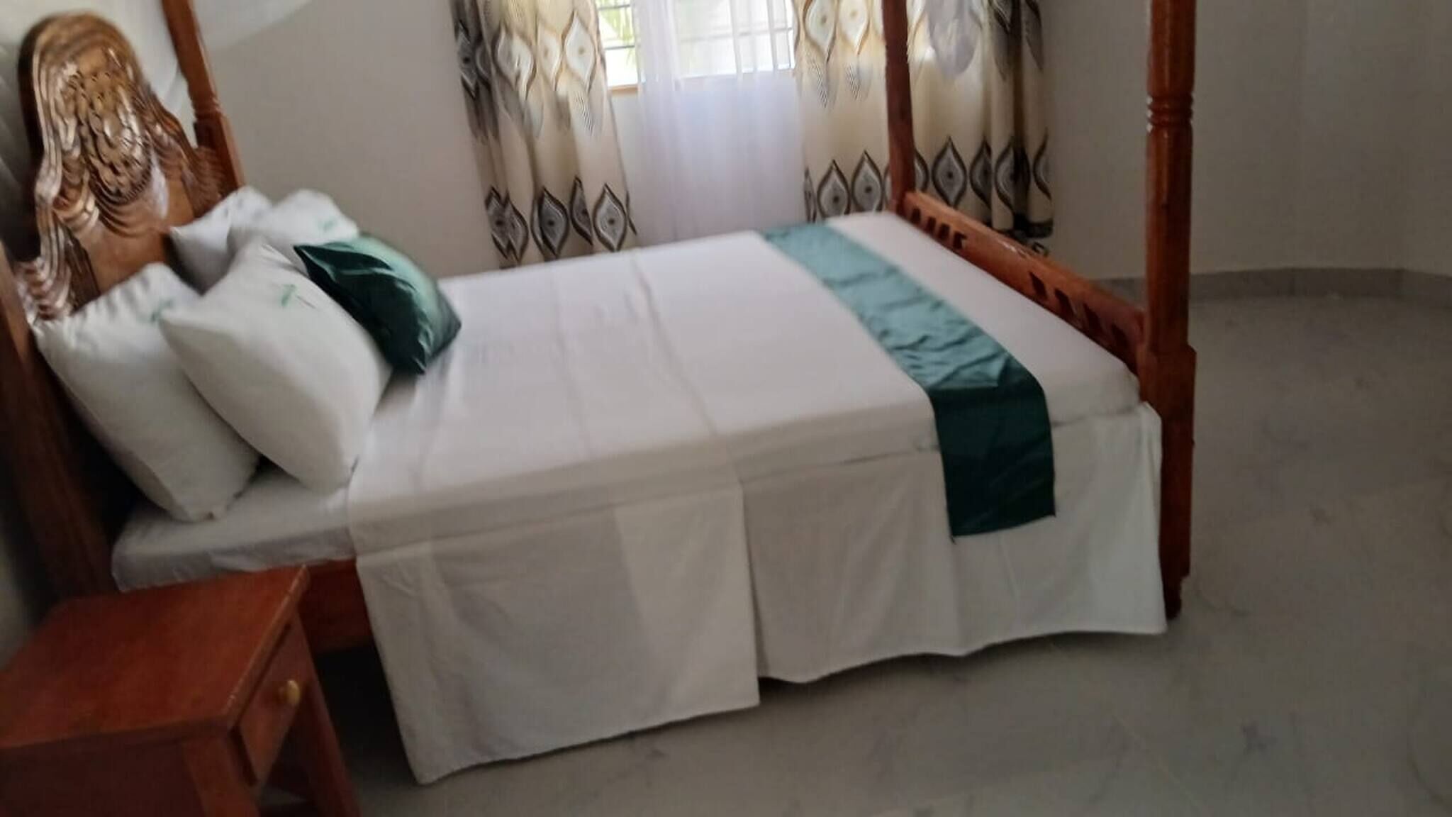A single bed with a wooden frame, white bedding, and a green accent.