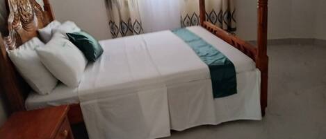 A single bed with a wooden frame, white bedding, and a green accent.