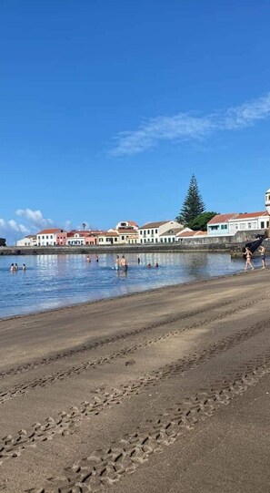 A beach with people swimming and walking along the shore. There are buildings with red roofs in the background.