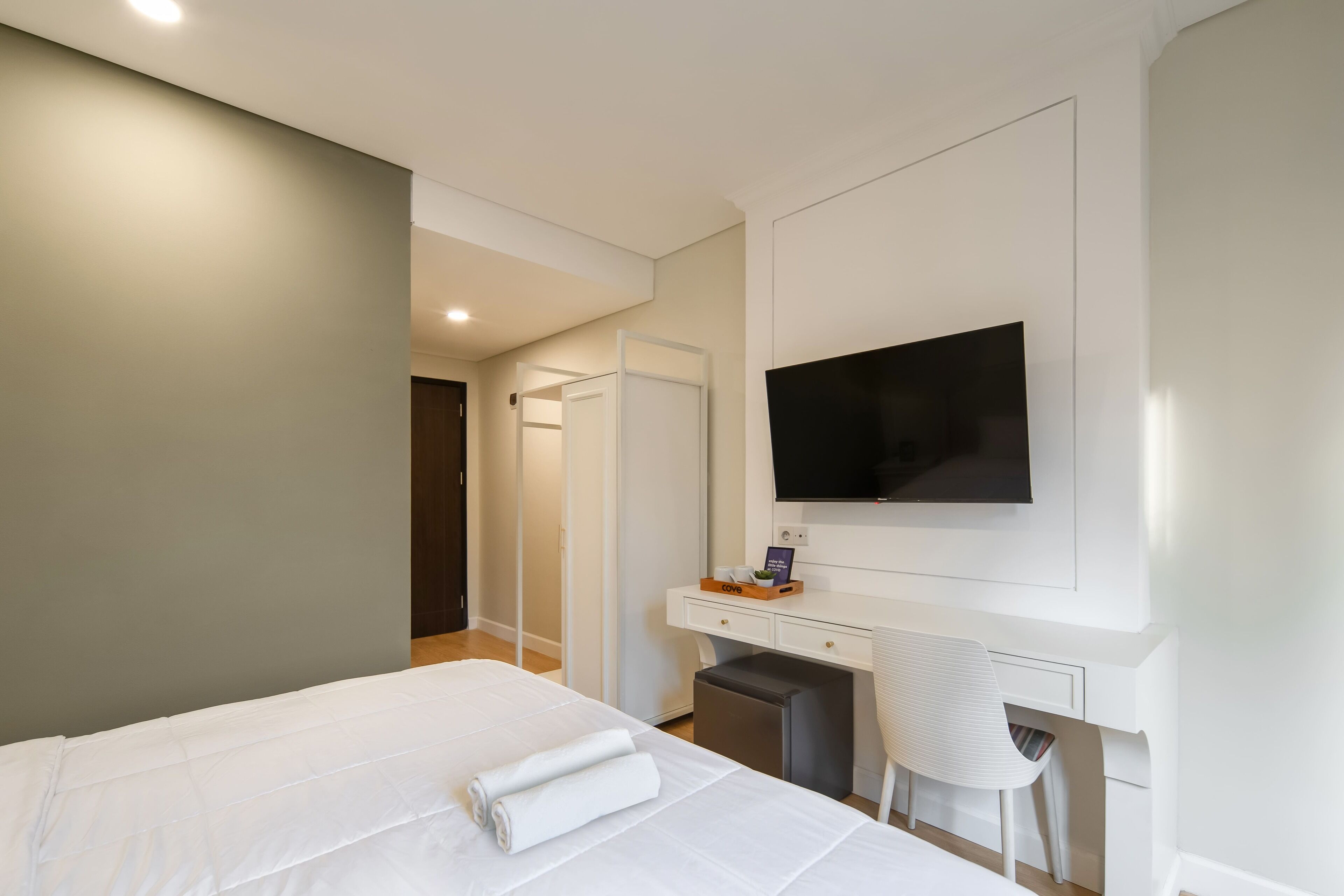 A modern hotel room with a large bed, a desk, a chair, a flat-screen TV, and a small table with a plant.