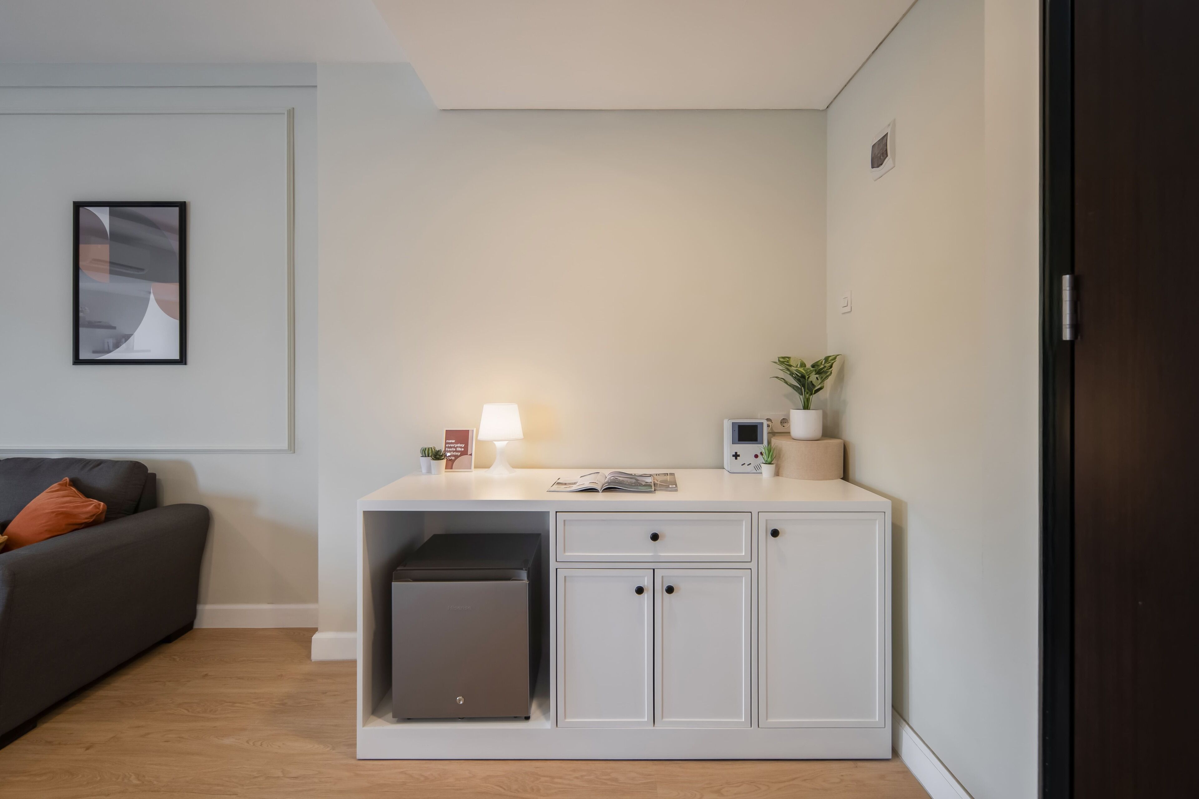 Un espace de vie compact comprenant un canapé, un petit meuble avec une imprimante, une lampe et une plante en pot.