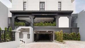 A modern hotel entrance with a covered driveway, a staircase, and a balcony with plants.