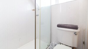 A bathroom with a glass shower enclosure, a toilet with a towel rack, and a white wall.