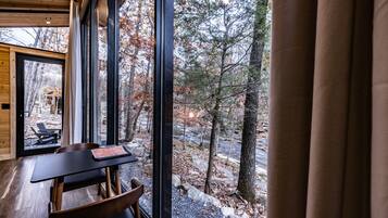 A wooden interior with a table and chairs, large windows, and a view of a forested area.