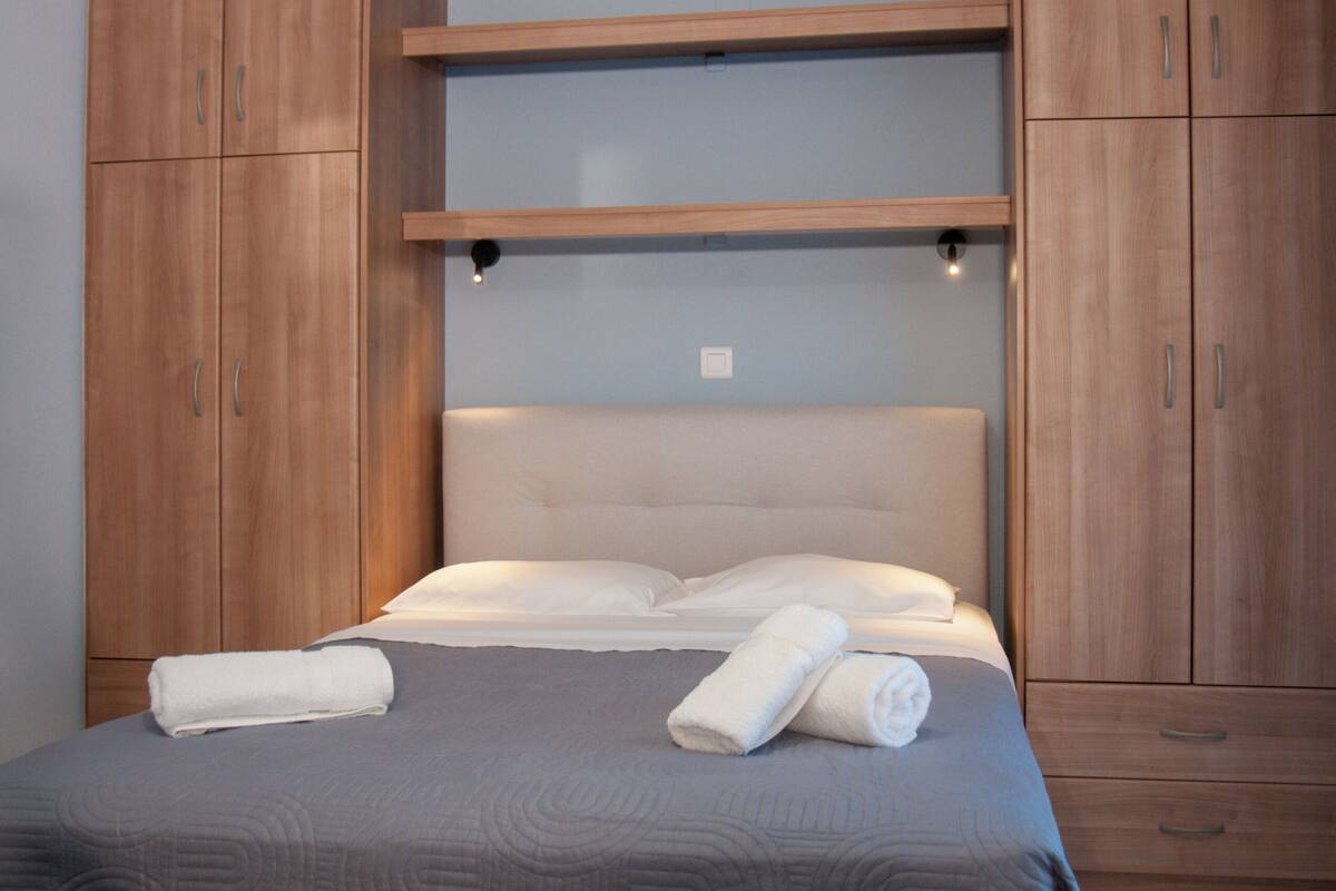 A bedroom with a bed, wooden wardrobe, and a ceiling light.