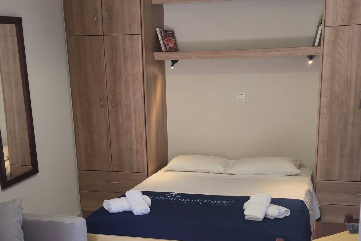 A bedroom with a bed, a wooden wardrobe, a bedside table, a chair, and a hanging light fixture.