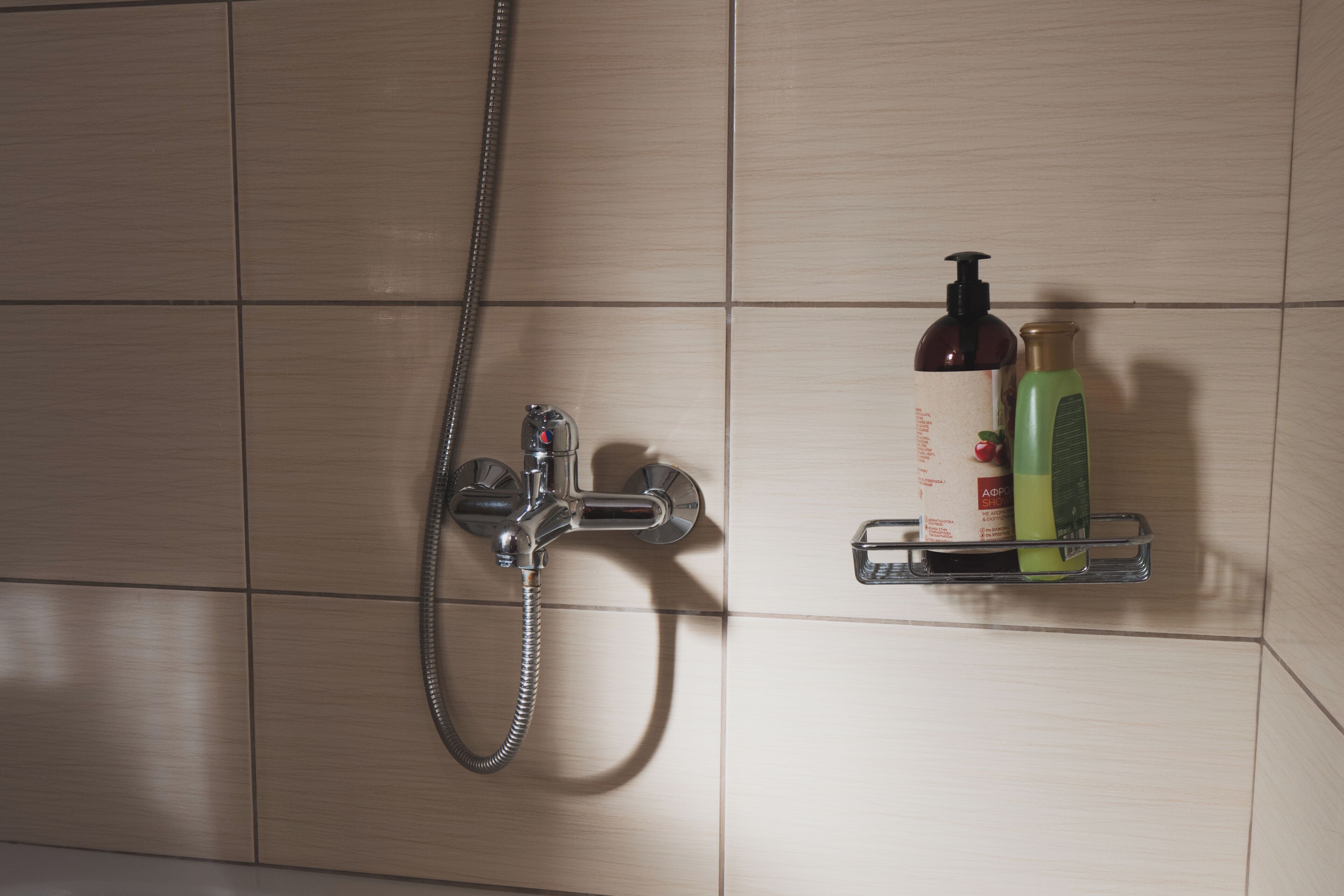 Une douche équipée d’un pommeau de douche à main et d’un robinet mural. On y trouve un distributeur de savon et une bouteille posée sur une petite étagère.