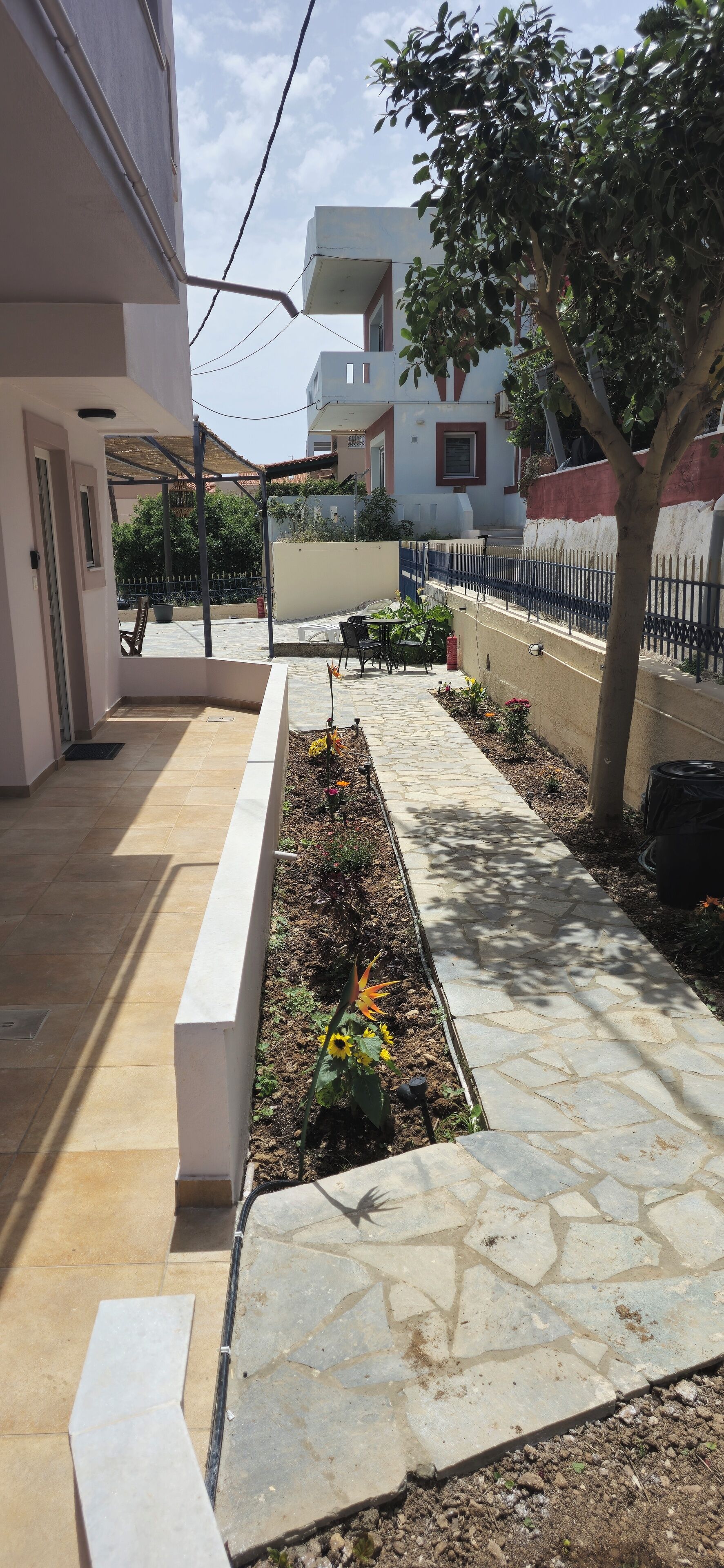 Un espace extérieur abrité, doté d’un sol carrelé, d’un jardinier avec des fleurs, d’un arbre et d’une clôture.