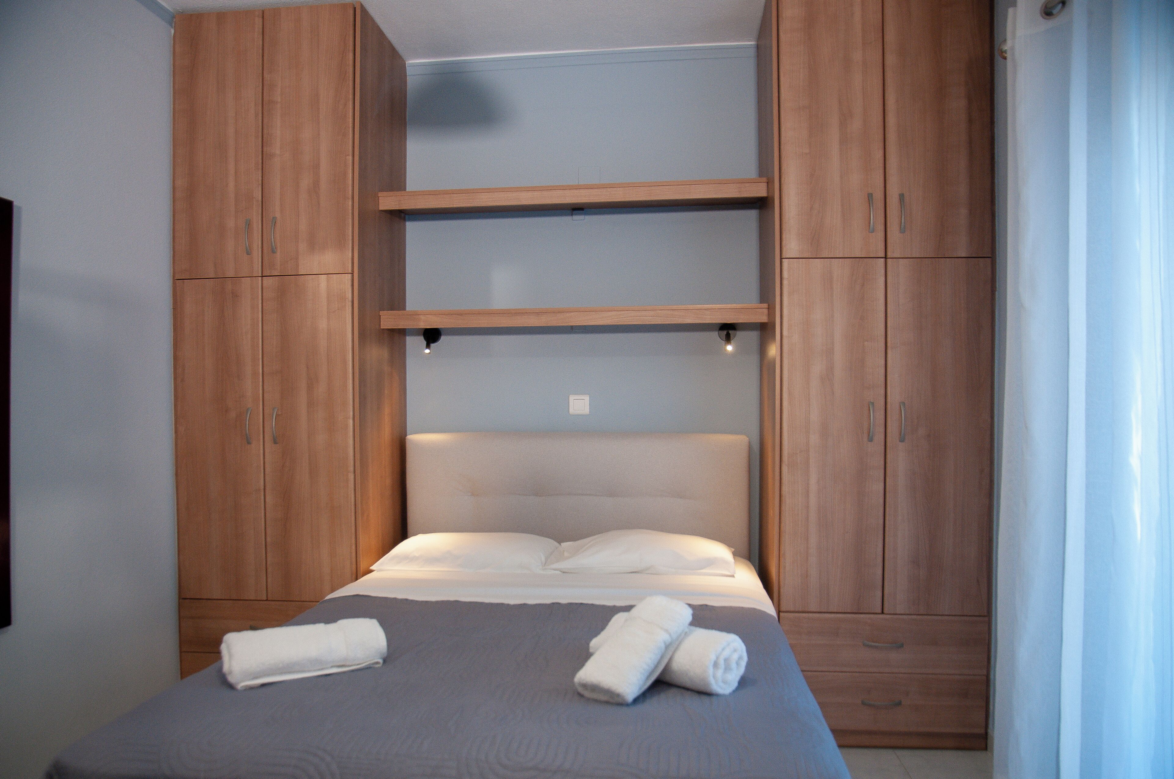 A bedroom with a bed, wooden wardrobe, and a shelf unit.