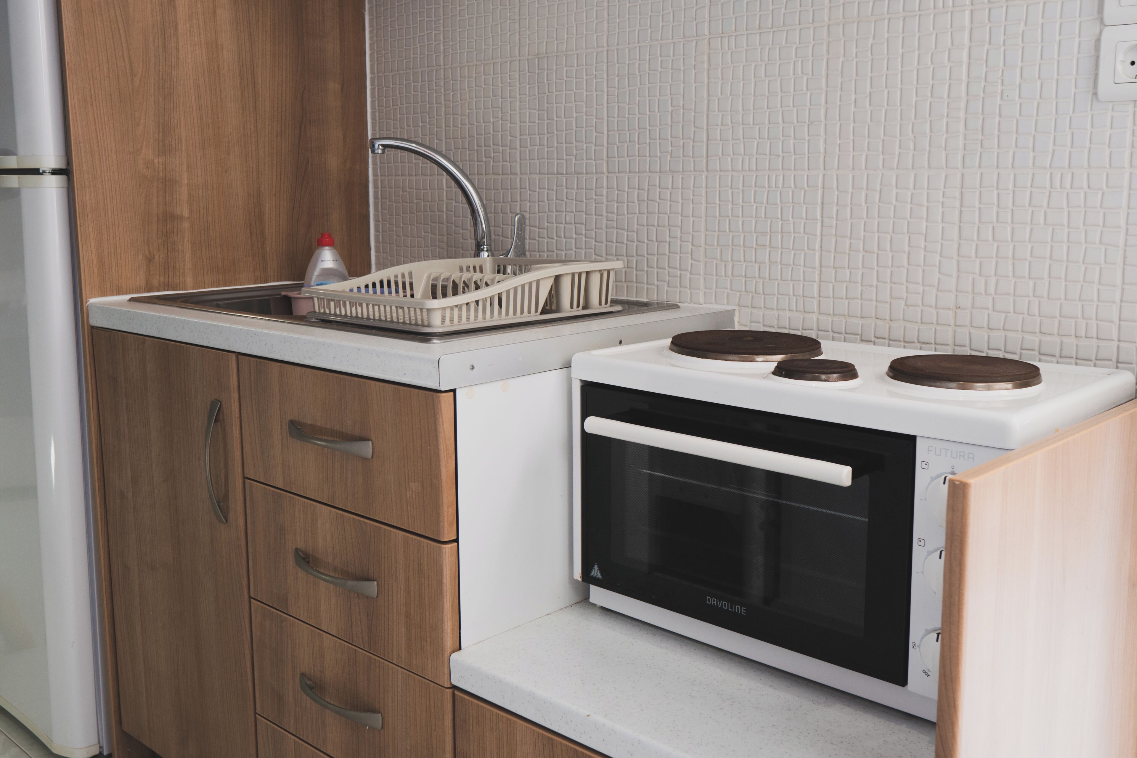 Una cocina compacta con horno integrado, un lavamanos con escurreplatos y armarios de madera.
