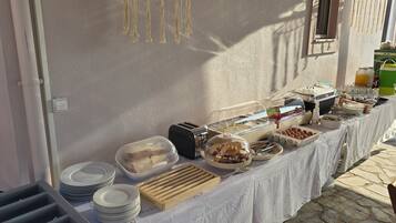 A buffet table with various food items and utensils, including bread, pastries, and a beverage dispenser.