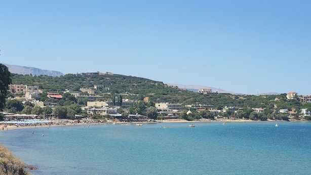 Un pueblo costero con playa, edificios y un paisaje montañoso al fondo.
