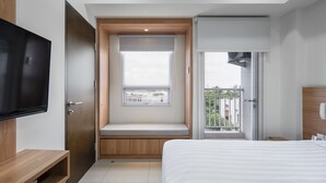 A modern hotel room with a large bed, a TV, a window seat, and a balcony with a view. - Cove Merakey (Cikarang)