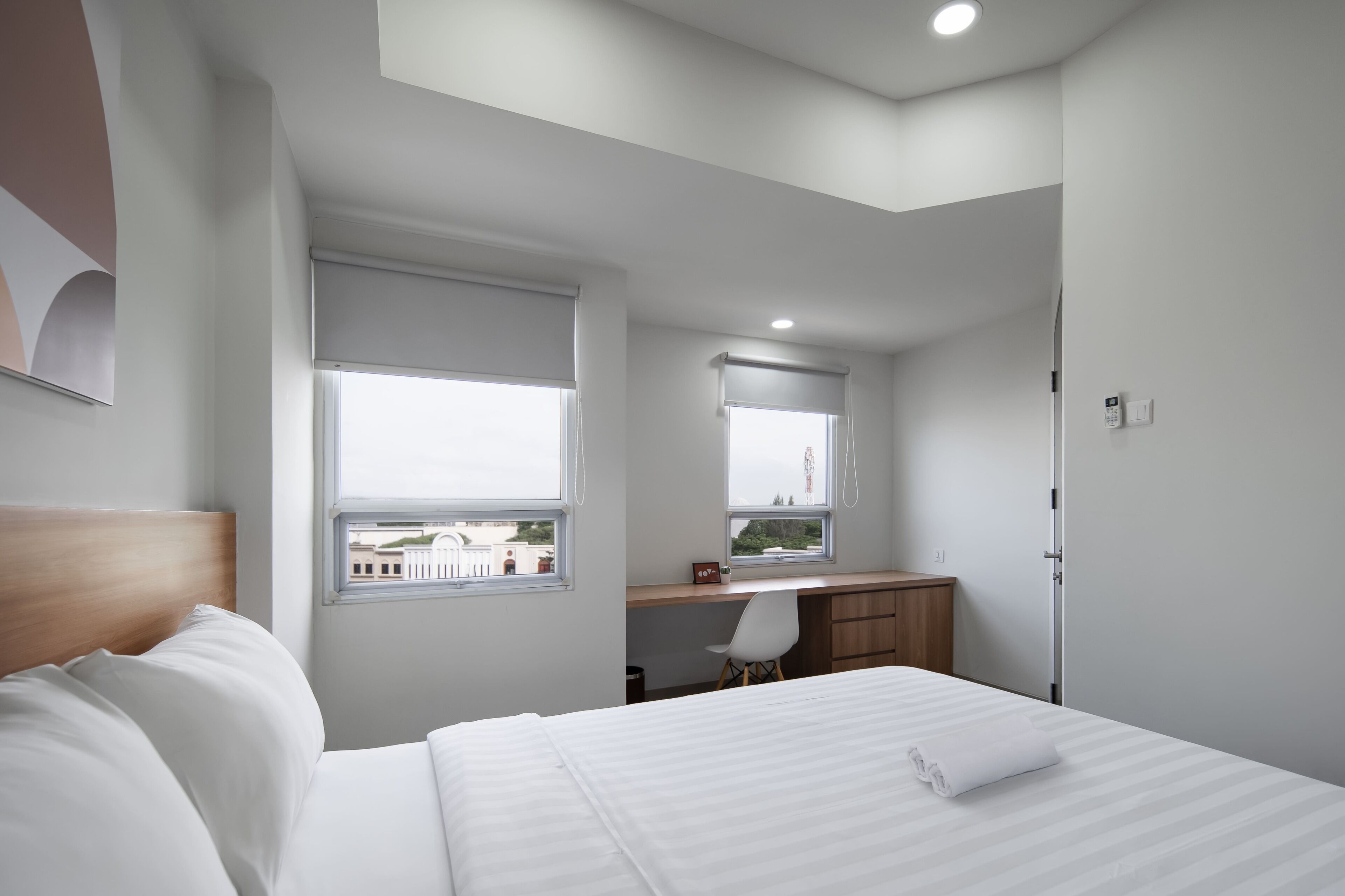 Una habitación de hotel moderna con una cama bien hecha, un escritorio con una silla y una ventana con persianas.